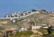 Small village and palestinian town on the hill behind israeli separation barrier on the West Bank in Israel.