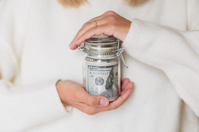 Young caucasian woman holding hands glass bank with cash money dollars bills Cindy Giovacchino on Women, Wealth, and the Future of Financial Mentorship