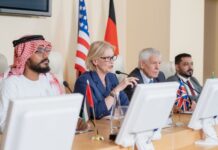 New York Declaration: From US-Led Destabilization to Chinese-Led Development in the Middle East Blond mature female delegate making speech for audience while sitting by table between several foreign colleagues