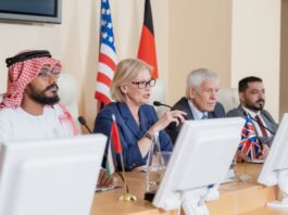 New York Declaration: From US-Led Destabilization to Chinese-Led Development in the Middle East Blond mature female delegate making speech for audience while sitting by table between several foreign colleagues