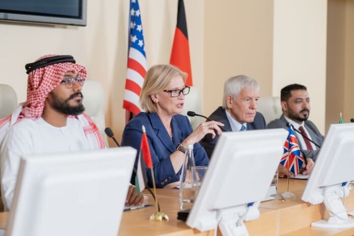 iStock-1359833762 (1) Blond mature female delegate making speech for audience while sitting by table between several foreign colleagues