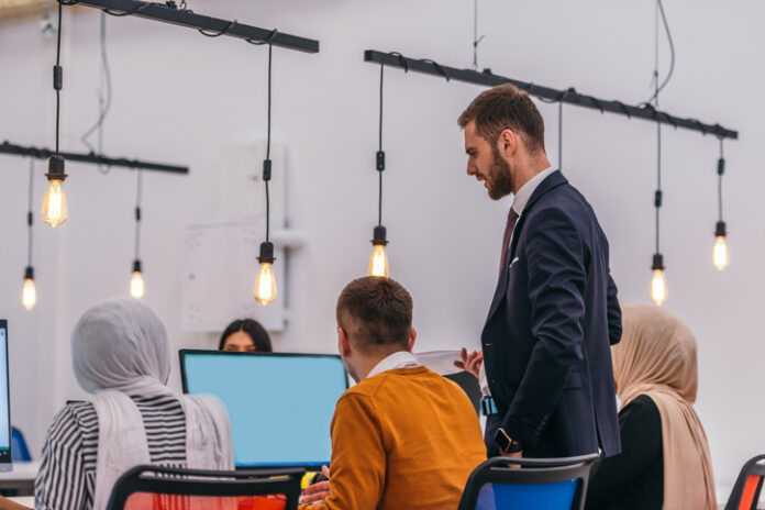 The manager is checking on his colleagues and is showing them what can be improved in their work. Manager teaching employees on incorporating AI in workflow