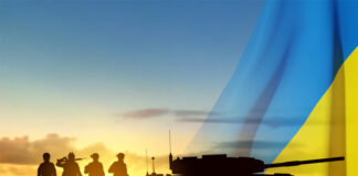Silhouettes of a soldiers and a main battle tank on a battlefield with Ukraine flag against the sunset.
