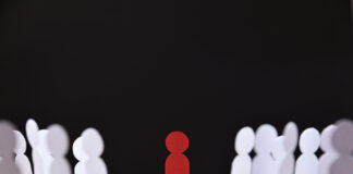 social discrimination concept with many little white paper men around a different one on wooden base and dark background front view