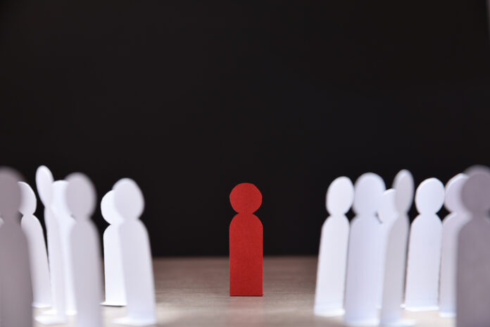 Social discrimination many paper men front dark social discrimination concept with many little white paper men around a different one on wooden base and dark background front view