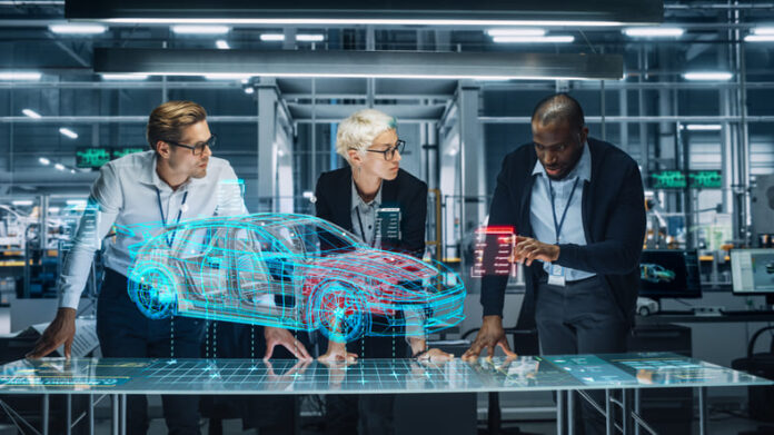 iStock-1353796860 (1) Diverse Team of Engineers Working in Office at Industrial Factory. Industrial Designers Discuss Electric Car Augmented Reality Hologramm. Specialists Work in Technological Car Development Facility.