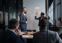 Business professionals in a modern office discussing artificial intelligence strategy. A woman wearing a VR headset gestures while presenting. Concept of innovation, technology, and AI integration.