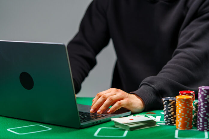 A player engages with online poker on a laptop, surrounded by colorful chips and playing cards on a green table Person playing casino online. Igaming industry concept.