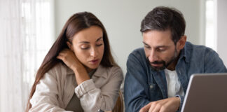 Wife and husband review financial documents seated at table with laptop, check receipts, discussing invoices, education savings or new rates.