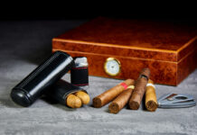 Six Cuban cigars on a stone table with a lighter, cutter and a wooden humidor