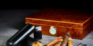 Six Cuban cigars on a stone table with a lighter, cutter and a wooden humidor