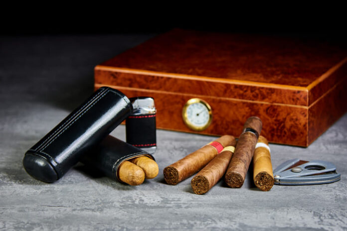iStock-1087519778 (1) Six Cuban cigars on a stone table with a lighter, cutter and a wooden humidor