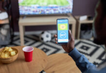 Amendments Strengthening South Africa’s Voluntary Exclusion System. Close up of male hand holding smartphone with online sports bets on screen while watching football match at home,