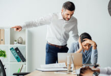 Selective focus of businessman pointing with finger near offended mexican colleague in office. Workplace Misconduct concept