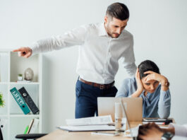 Selective focus of businessman pointing with finger near offended mexican colleague in office. Workplace Misconduct concept