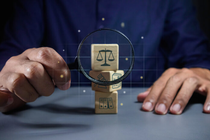 Man holding a magnifying glass to look at wooden blocks with law or legal symbol.