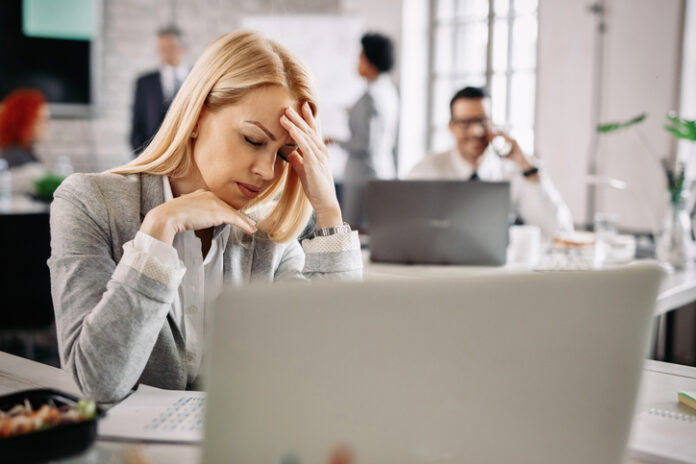 Businesswoman experiencing a strong headache while working in the office. Stressed businesswoman holding her head in pain and having headache at work.