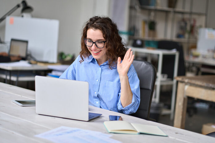Happy young business woman employee, hr manager having remote online work hybrid meeting or distance job interview waving hand looking at laptop during virtual video conference call in office.