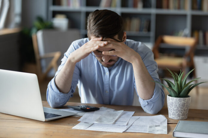 Frustrated young man grabbing head in despair checking finance documents Return-to-office mandate affects the finance of employee