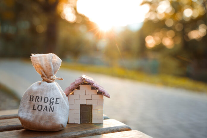 Bridge loan concept - is a short-term loan secured by real estate.Money bag and miniature house in the park in the sunset light. Real estate and finance Bridge loan concept