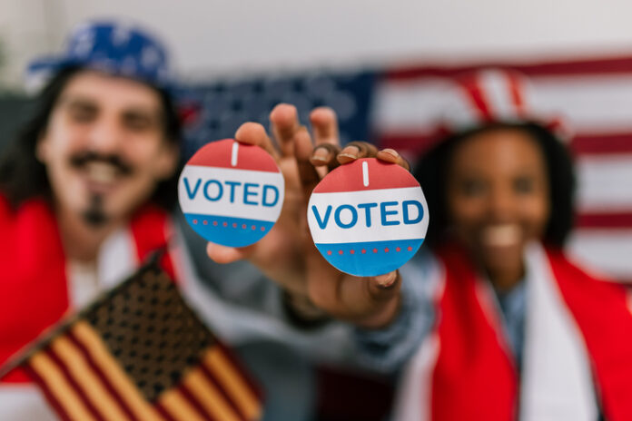 Multiracial Couple Celebrates Voting in America voting in the U.S., wearing American flag caps and showing happiness and civic pride while watching the elections.